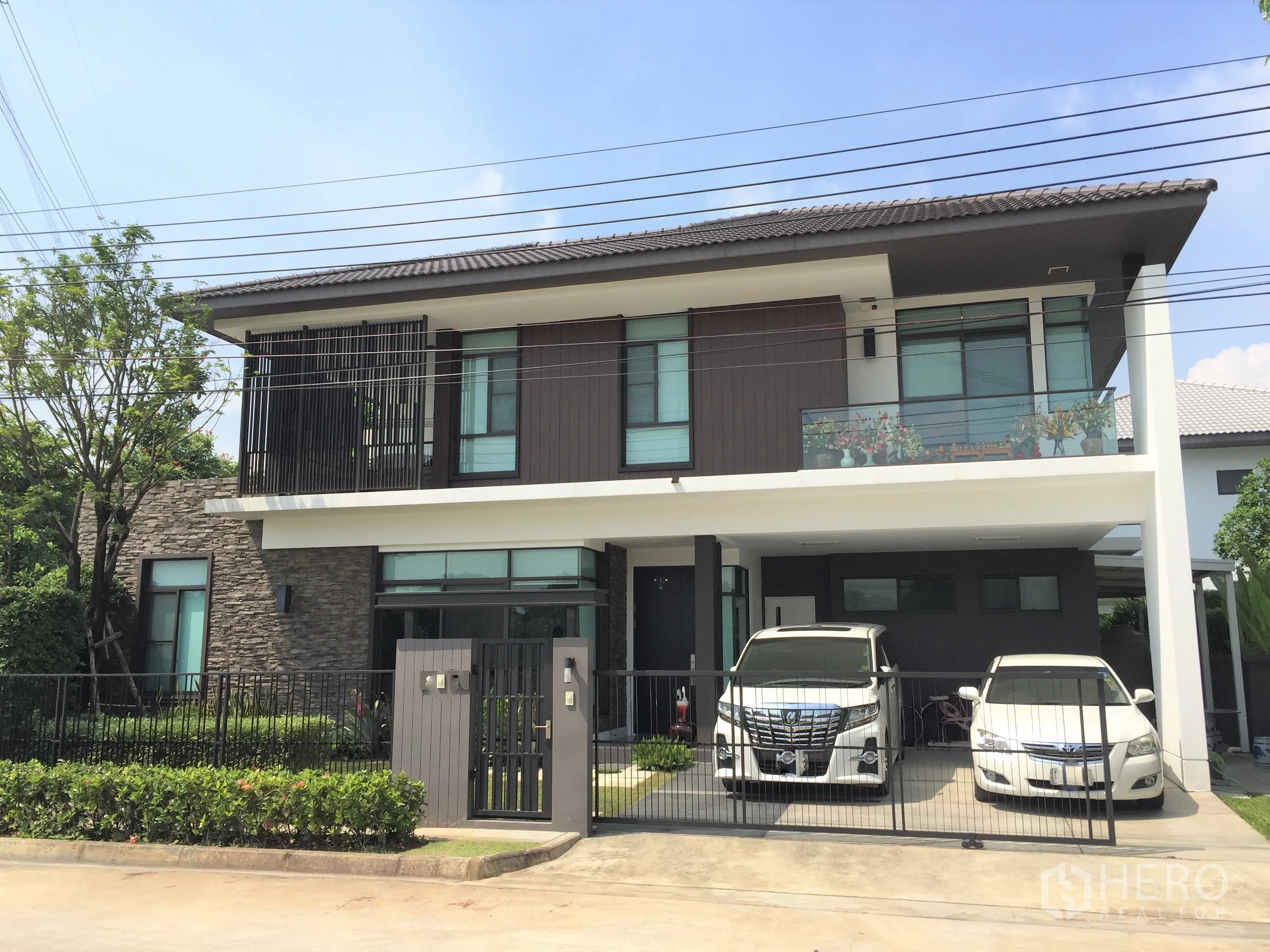 独立式住宅 出租或出售在Prawet, Bangkok - 现代两层独栋外观，石材立面、阳台与带门庭的双车位车棚。