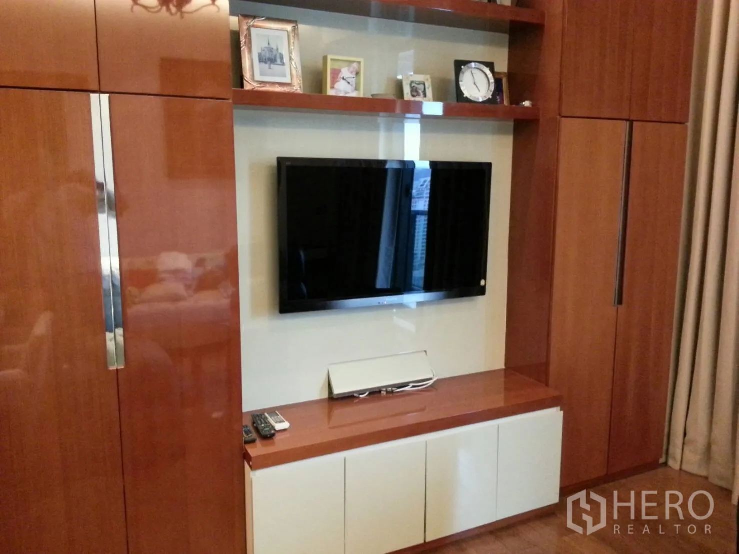 Condominium for rent or sale in Khlong Toei, Bangkok - Built-in wooden media wall with shelving and a flat-screen TV in the living area.