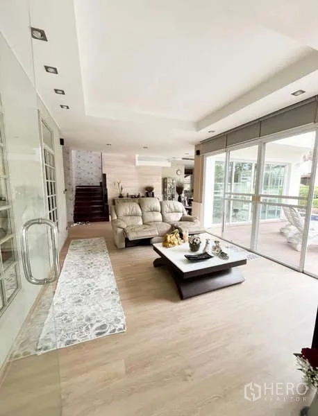 บ้าน ให้เช่าในBang Phli, Samut Prakan - ห้องนั่งเล่นโปร่งโล่ง ผนังกระจกบานเลื่อนเต็มสูง พื้นไม้ โซฟา และบันได