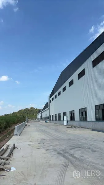货栈 出租在Ban Bueng, Chon Buri - 现代白色仓库侧立面，长车道与远处山景。