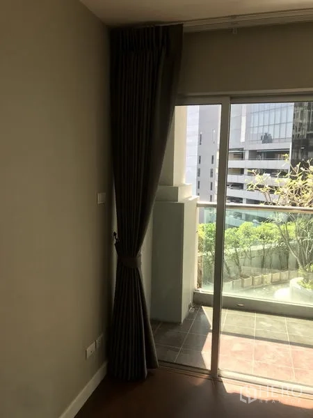 Condominium for rent or sale in Huai Khwang, Bangkok - Sliding glass door to a balcony with city view and greenery beside dark blackout curtains.