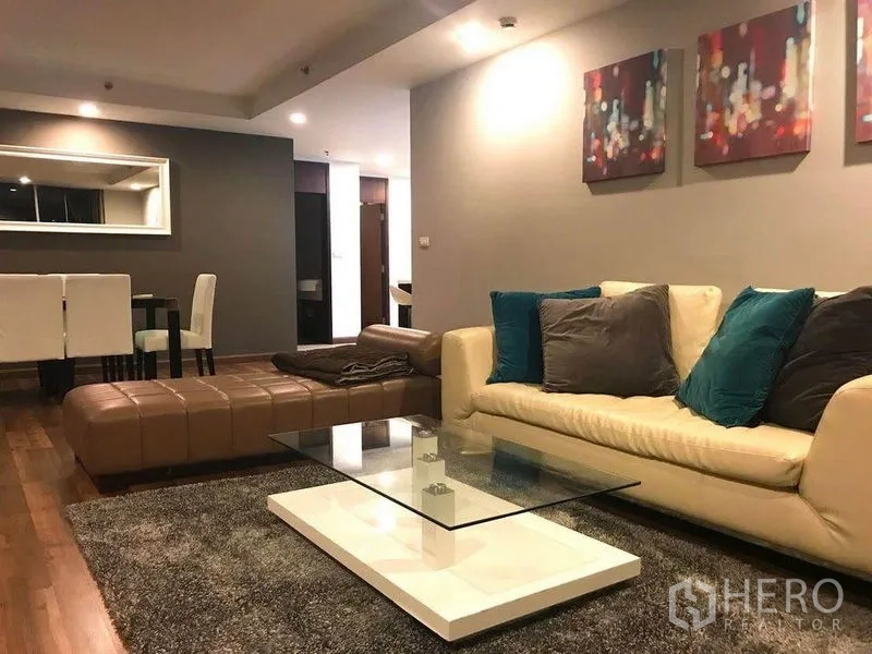 公寓 出租在Pathum Wan, Bangkok - 温馨客厅，皮沙发、脚凳、玻璃茶几与墙面艺术装饰