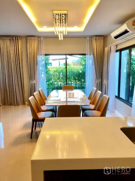 Detached House for rent in Bang Kapi, Bangkok - Dining area for eight beneath a chandelier, beside sliding doors and the kitchen counter.