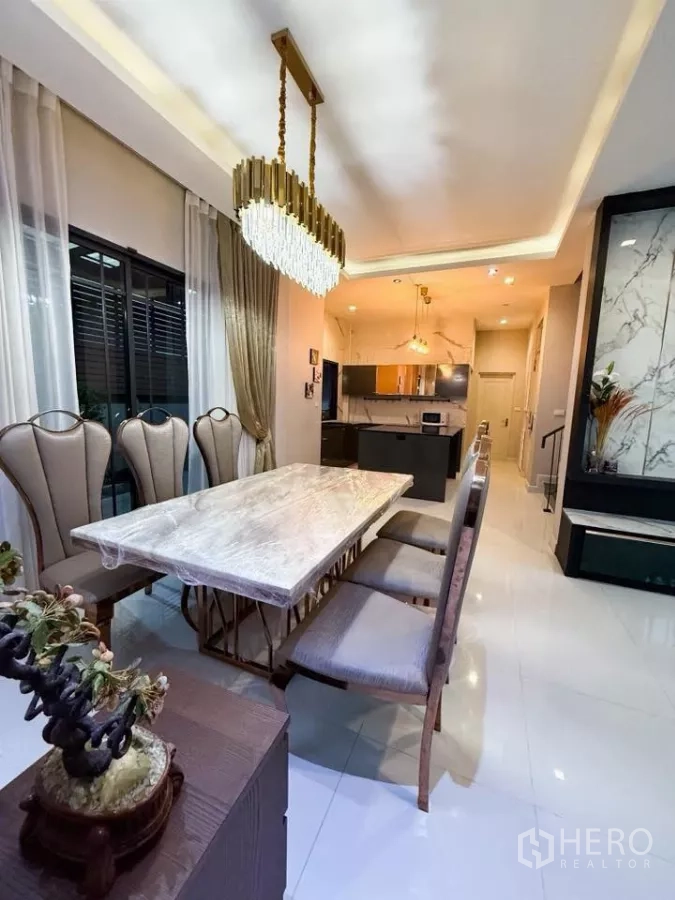 Detached House for rent or sale in Bang Phli, Samut Prakan - Long view of the dining area with crystal chandelier, six high‑back chairs and tall drapes.