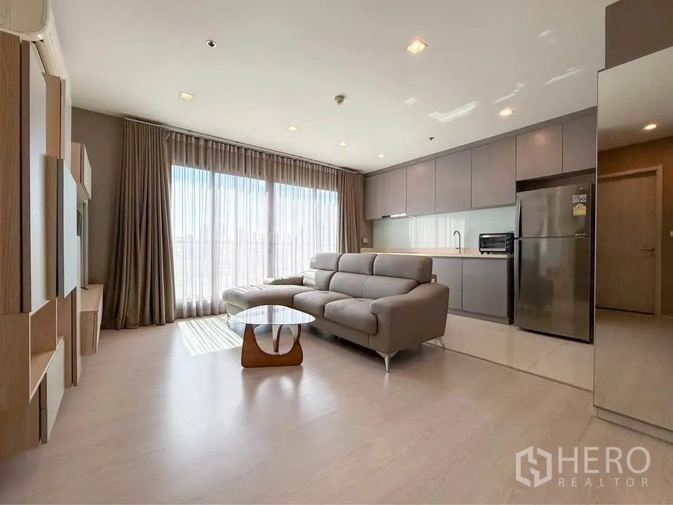公寓 for rent in Khlong Toei, Bangkok - 开放客厅设大窗、沙发与一字型厨房及冰箱。