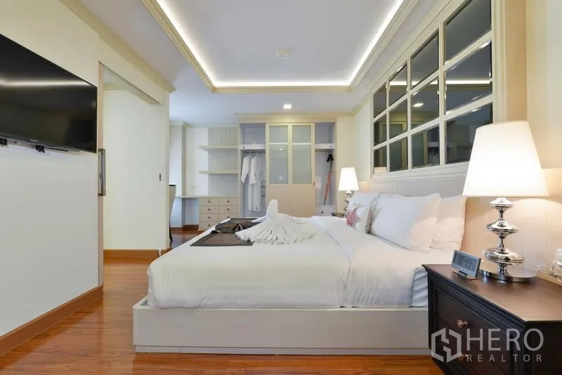 Apartment for rent in Khlong Toei, Bangkok - Spacious bedroom showing built-in wardrobe, study nook, bedside lamps, and wall-mounted TV.