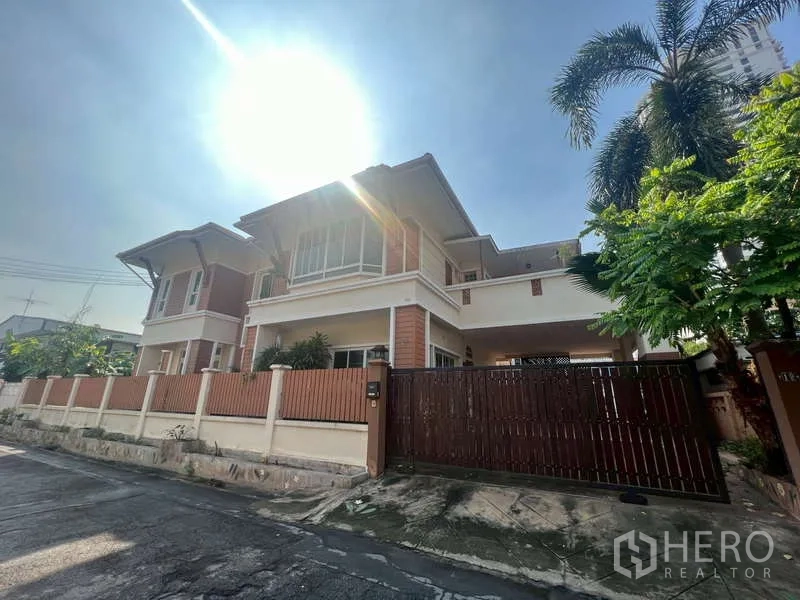 Detached House for rent in Watthana, Bangkok - Two-storey detached house with wooden fence and gate under bright sun on a quiet street.