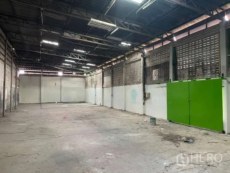 Warehouse for rent in Nong Khaem, Bangkok - Long storage hall with vented walls and bright green steel double doors.