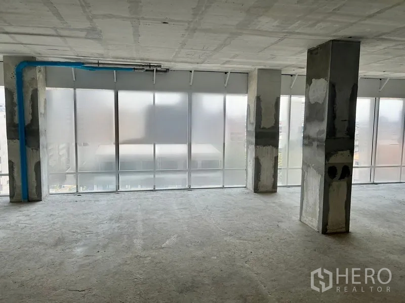 办公空间 出租在Sathon, Bangkok - 角落办公区域，磨砂落地玻璃、混凝土立柱与可见蓝色管线。