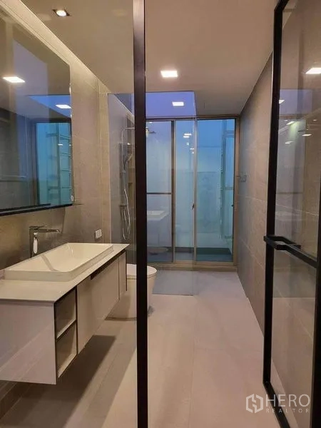 Detached House for rent in Saphan Sung, Bangkok - Contemporary bathroom with large mirror, wall‑mounted vanity, glass shower enclosure and neutral tiles.