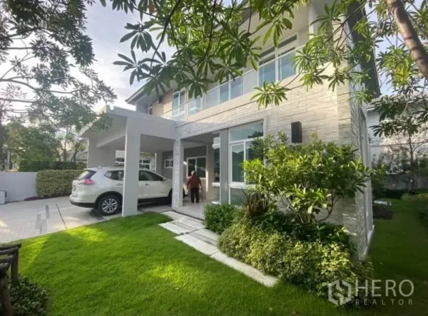 独立式住宅 出租在Prawet, Bangkok - 侧面视角，展示有顶车棚与修剪整齐的草坪与灌木。