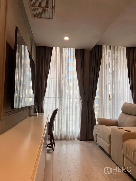 公寓 出租在Pathum Wan, Bangkok - 客厅电视柜与工作桌，面向大面积窗户与深色窗帘