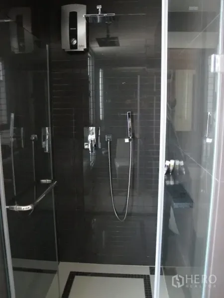 Condominium for rent or sale in Khlong Toei, Bangkok - Modern shower enclosure with dark tiles, rain shower, and water heater.