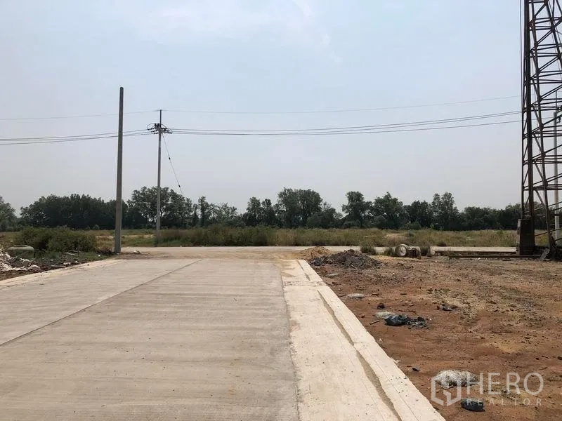 Land for sale in Mueang Samut Sakhon, Samut Sakhon - Concrete access road facing a green field with overhead power lines and a level, cleared plot.