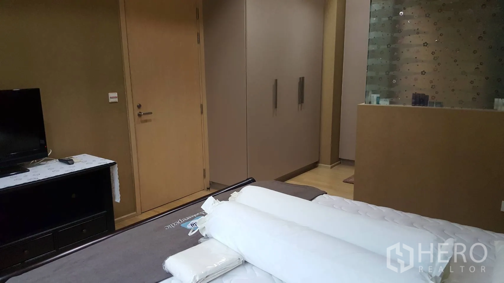 Condominium for rent in Khlong Toei, Bangkok - Bangkok condo bedroom with built-in wardrobe, TV console and frosted glass partition.