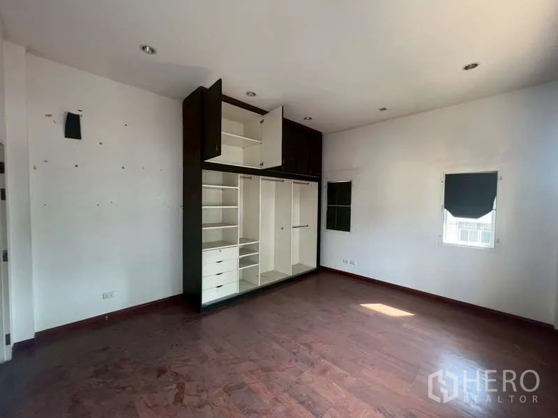 Detached House for rent in Watthana, Bangkok - Spacious bedroom with built-in wardrobe, white walls and wood flooring.