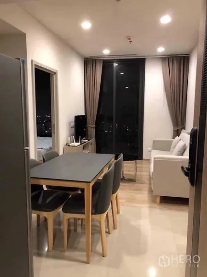 Condominium for rent in Khlong Toei, Bangkok - Alternate view of dining and living space leading to balcony with night skyline.