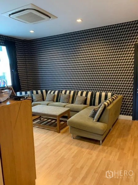 Townhouse for rent or sale in Chatuchak, Bangkok - Family lounge with L‑shaped sofa, wood floors and patterned accent wall.