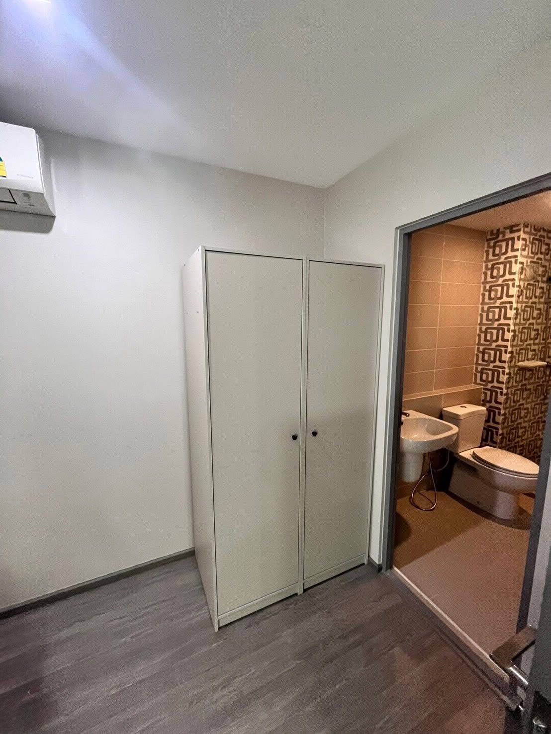 Townhouse for rent or sale in Lat Phrao, Bangkok - Compact room with wardrobe opening to an ensuite bathroom with patterned tiles and sanitary ware.