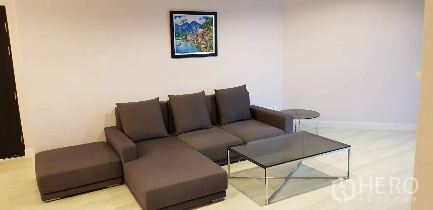Condominium for rent in Huai Khwang, Bangkok - Bright living room with a gray L-shaped sofa, glass coffee table and light wood flooring.