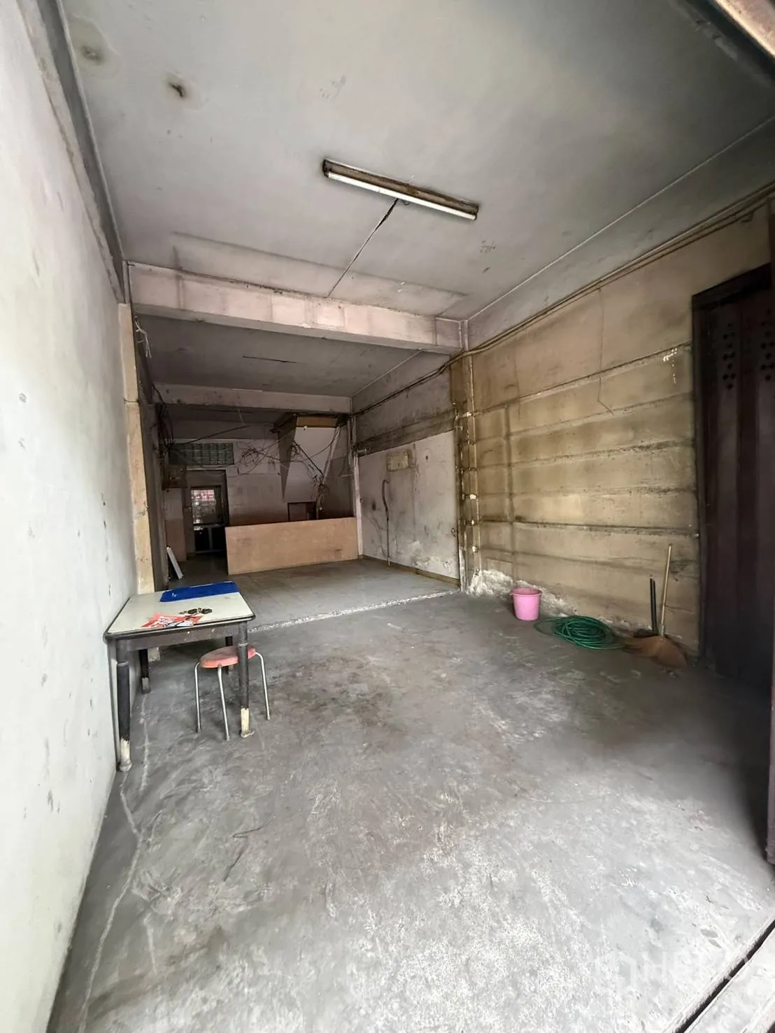 Shophouse for rent in Khlong Toei, Bangkok - Open ground-floor space with concrete floor, fluorescent light, and a sliding metal gate.