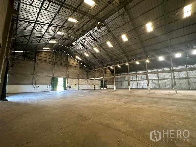 Warehouse for rent in Mueang Pathum Thani, Pathum Thani - Corner view of the warehouse showing bright ceiling lights, ventilation panels and wide entry door.