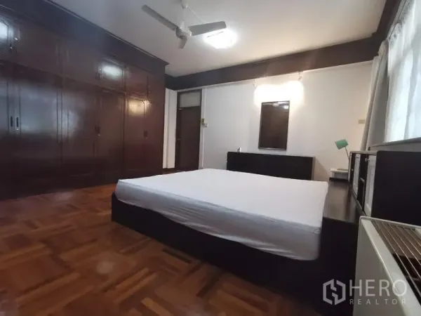 Apartment for rent in Khlong Toei, Bangkok - Primary bedroom with large built-in wardrobes, ceiling fan and parquet flooring.