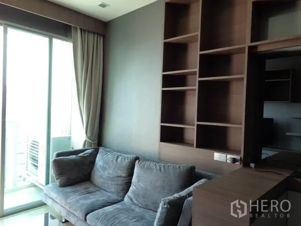คอนโด ให้เช่าในWatthana, Bangkok - ห้องนั่งเล่นสว่าง โซฟาสีเทา หน้าต่างบานใหญ่เปิดสู่ระเบียง พร้อมชั้นบิวต์อินไม้