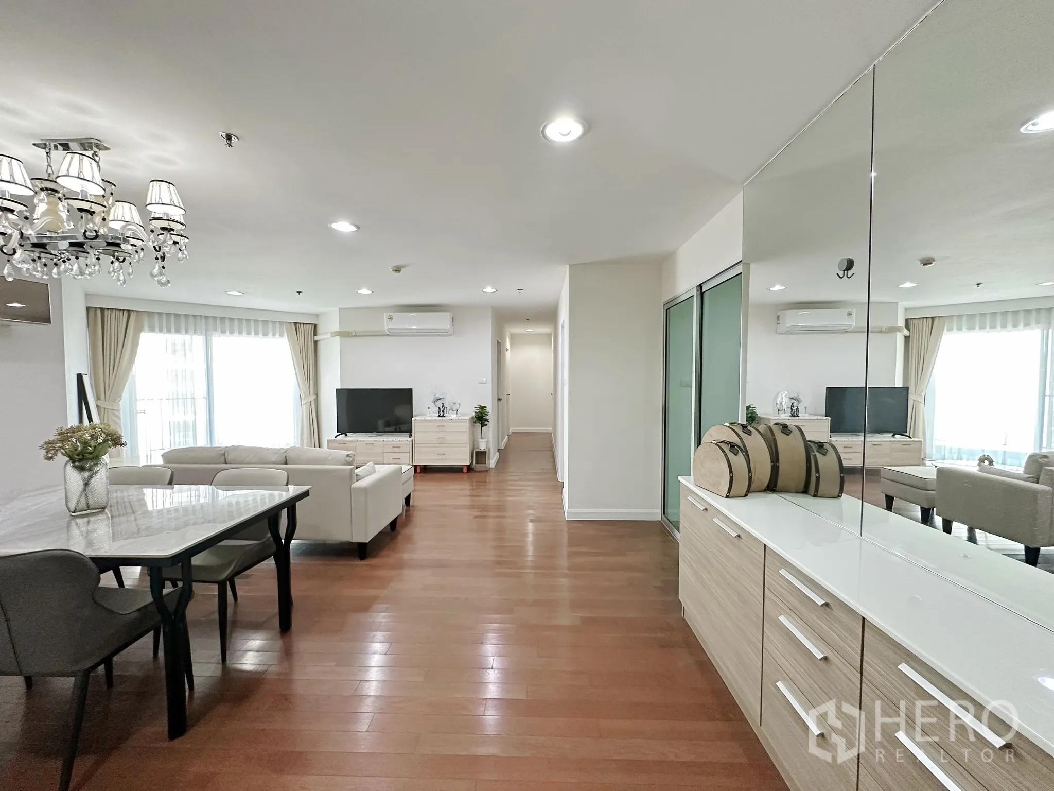 Condominium for sale in Huai Khwang, Bangkok - Another angle of the living space showing mirrored cabinetry, dining table, sofa, and bright windows.