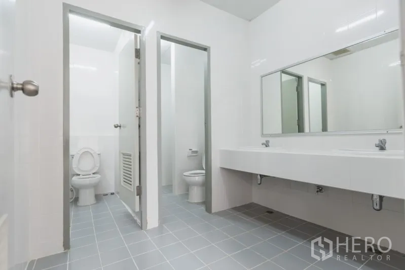 Factory for rent in Si Racha, Chon Buri - Clean tiled restroom with two toilet stalls, a long mirror, and twin sinks.