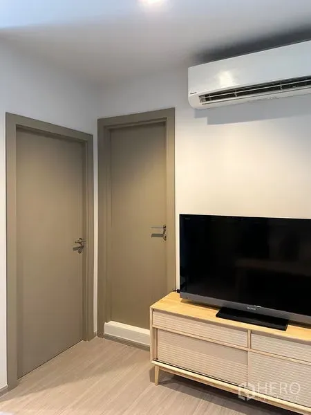 公寓 出售在Ratchathewi, Bangkok - 紧凑客厅，挂壁空调、两扇室内门与木质电视柜上的电视。