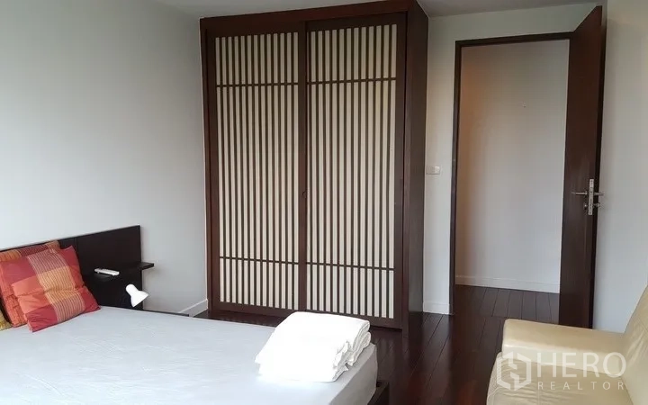 Condominium for rent in Khlong Toei, Bangkok - Bright bedroom with wooden flooring, a slatted sliding wardrobe, and a double bed with colorful cushions.