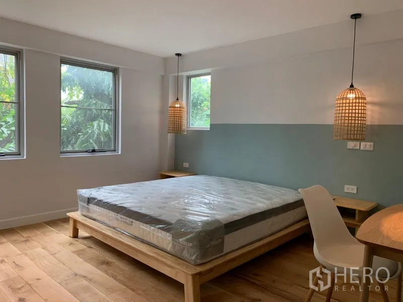 Condominium for sale in Watthana, Bangkok - Primary bedroom with platform bed, woven pendant lights and garden outlook.