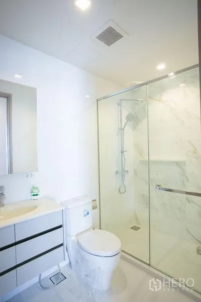 Condominium for rent in Watthana, Bangkok - Bright bathroom with glass-enclosed shower, toilet and white vanity.