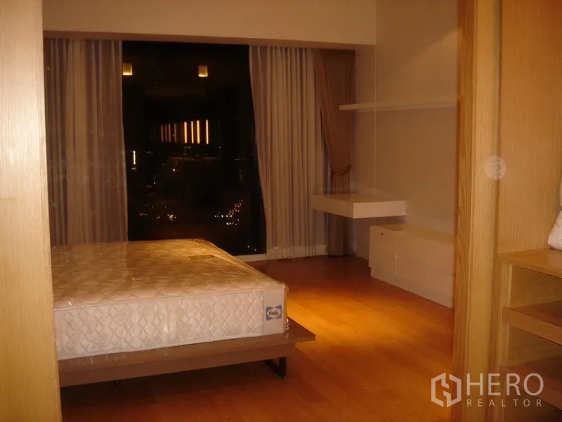 Condominium for rent in Sathon, Bangkok - Cozy bedroom at night with bed, curtains and floating work desk.