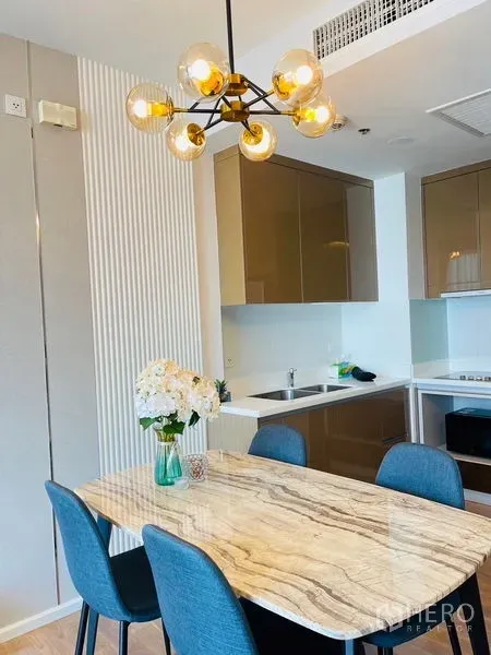 Condominium for rent in Khlong Toei, Bangkok - Marble-top dining table beside a modern kitchen with glossy cabinets and a designer chandelier in a Khlong Toei condominium.