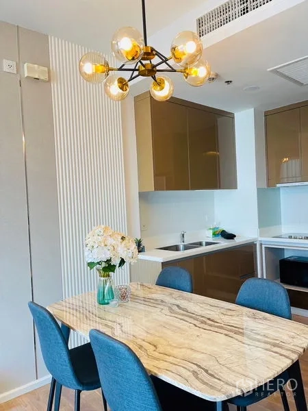 Condominium for rent in Khlong Toei, Bangkok - Marble-top dining table beside a modern kitchen with glossy cabinets and a designer chandelier in a Khlong Toei condominium.