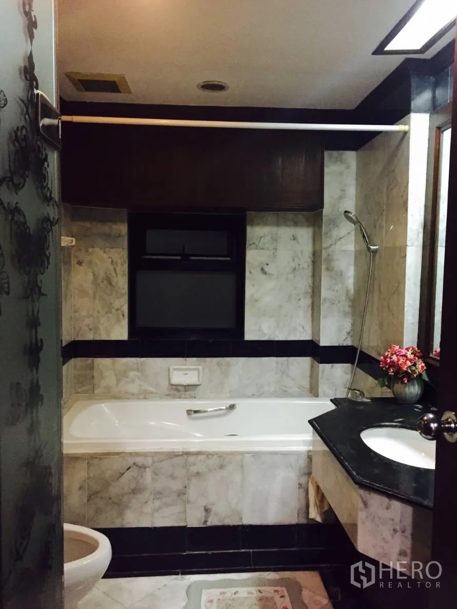 Condominium for rent in Sathon, Bangkok - Bathroom with marble tiles, bathtub with handheld shower and black countertop vanity.