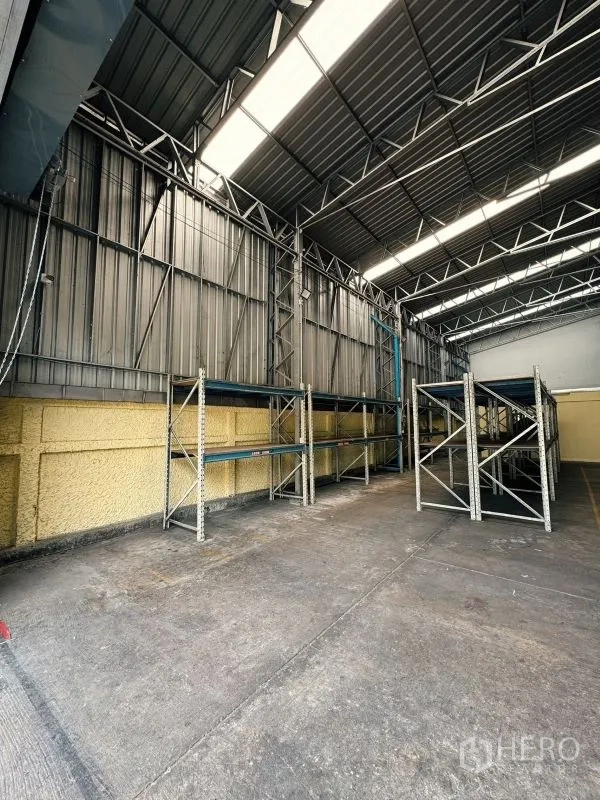 货栈 出租在Din Daeng, Bangkok - 仓库内部，高挑钢桁架屋顶与采光带，混凝土地面和货架系统。