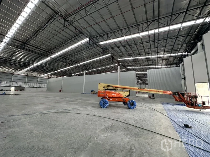 工厂 出租在Khlong Luang, Pathum Thani - 开阔生产区，臂式升降车在钢结构屋顶下作业。