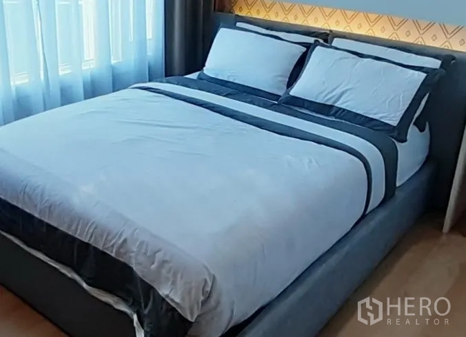 Condominium for rent in Khlong Toei, Bangkok - Cozy bedroom with upholstered queen bed, layered bedding and soft daylight from sheer curtains.