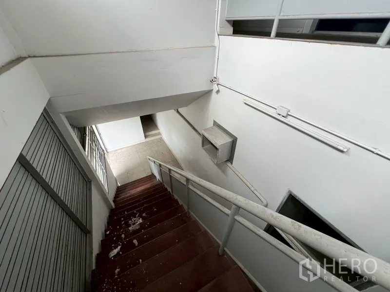 Shophouse for rent in Phra Khanong, Bangkok - View down a staircase with metal railing and an electrical box on the wall.