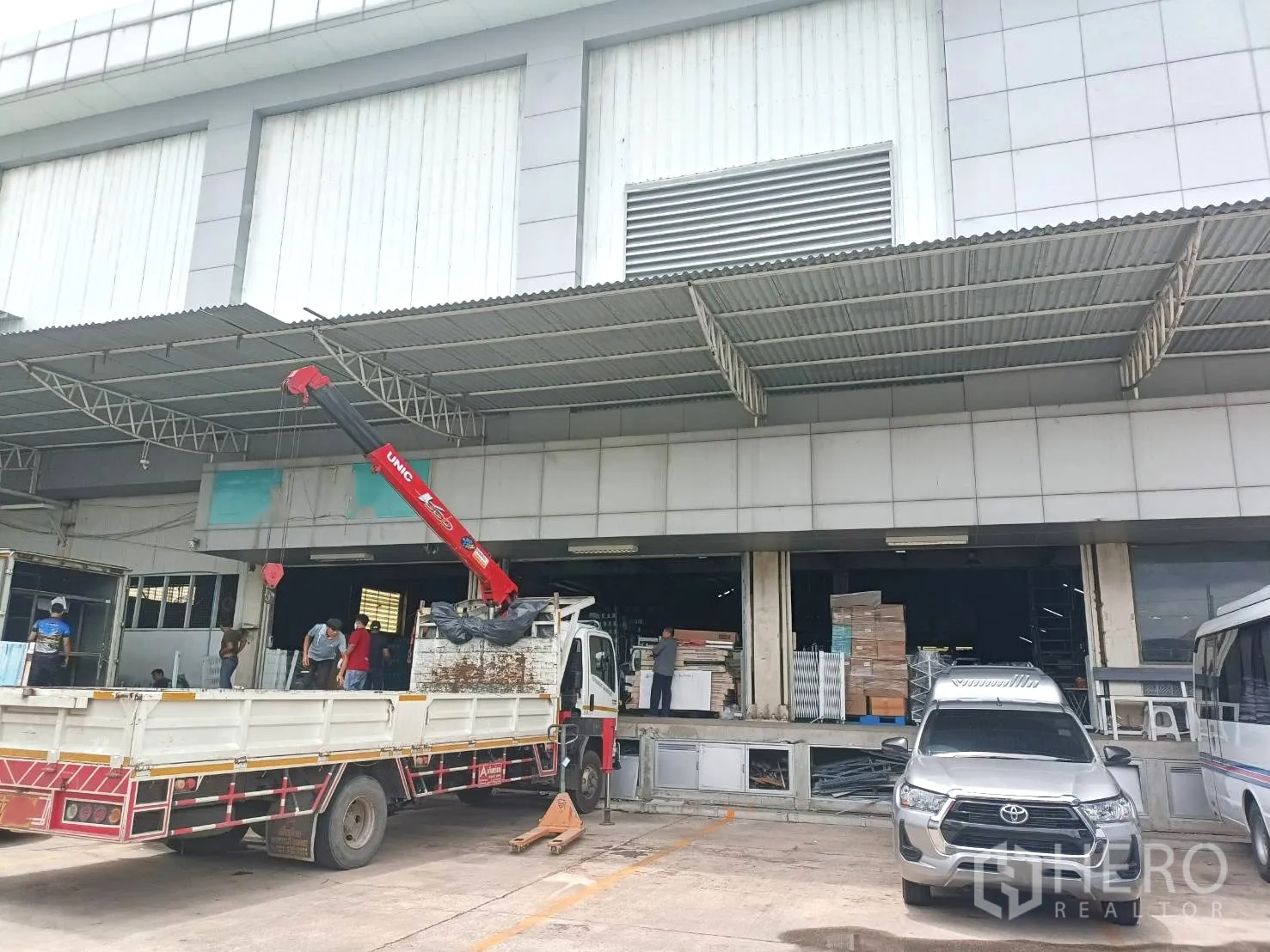 Warehouse for rent in Lam Luk Ka, Pathum Thani - Canopied loading docks with a crane unloading materials to the warehouse openings.