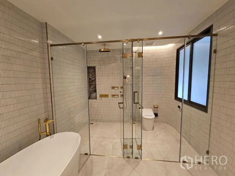 Detached House for rent in Wang Thonglang, Bangkok - Luxurious bathroom with freestanding tub and glass shower enclosure with gold fittings.