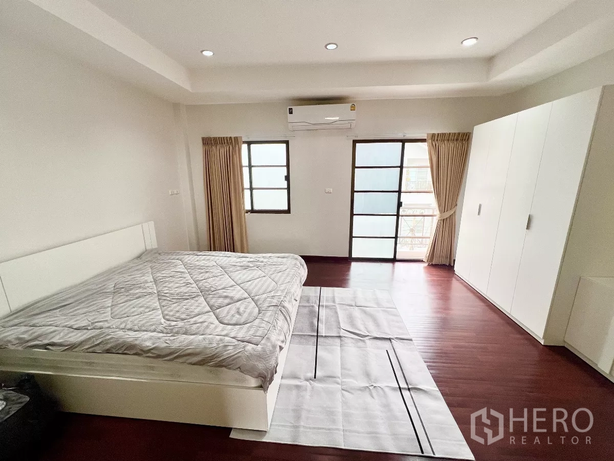 Townhouse for rent or sale in Phra Khanong, Bangkok - Primary bedroom with king bed, wardrobes, balcony doors and wood flooring.