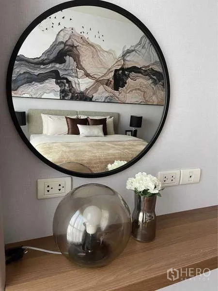 Condominium for rent in Pathum Wan, Bangkok - Round mirror above console reflecting the bedroom with art headboard and neutral decor.
