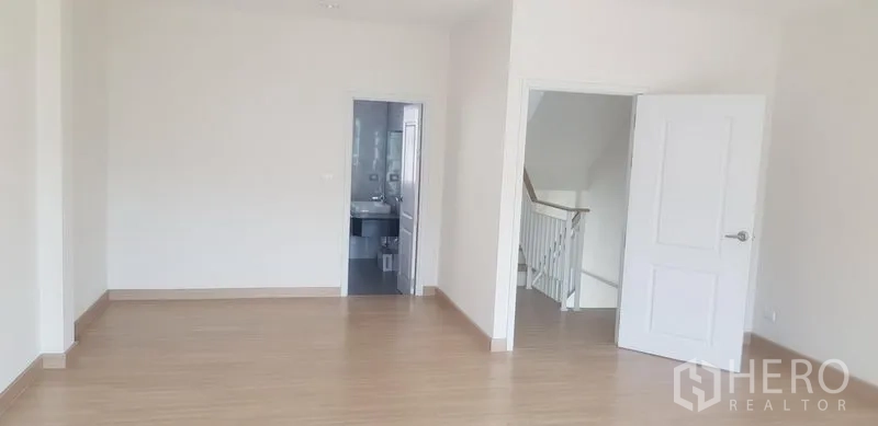 联排别墅 出租在Bang Na, Bangkok - 大卧室，浅色木地板，白色房门，并可进入套内卫生间。