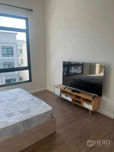 Townhouse for rent in Suan Luang, Bangkok - Sunny bedroom with bed, large window, wood flooring and TV on a low console.