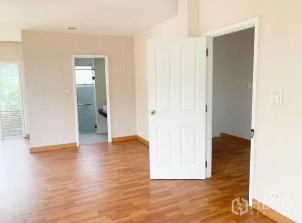Detached House for sale in Saphan Sung, Bangkok - Spacious upstairs room with wood flooring, open door to a bathroom and adjoining room.