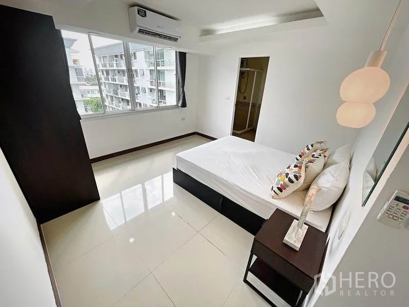 Condominium for rent in Khlong Toei, Bangkok - Secondary bedroom with big window, bedside table and doorway to an ensuite bathroom.